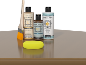 Retique It® Pecan Multipurpose Kit contents with Light Wood Liquid Wood primer, Pecan gel stain alternative, Tripletique gloss interior top coat, paintbrush, and yellow sponge displayed on a wood surface.