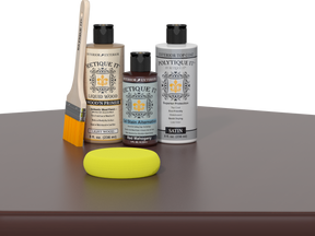 Retique It® Light Wood Wood’n Primer with Red Mahogany Gel Stain Alternative, satin topcoat, brush, and yellow sponge on a tabletop.