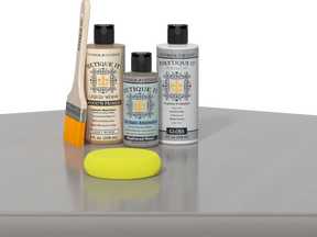 Retique It® Weathered Wood kit with brush, Wood’n Primer, Weathered Wood stain alternative, gloss top coat, and yellow sponge on a reflective surface.