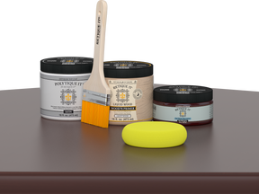 Retique It® Red Mahogany Multipurpose Kit contents with Liquid Wood primer, Red Mahogany gel stain alternative, PolyTique It® satin exterior top coat, paintbrush, and yellow sponge displayed on a dark wood surface.