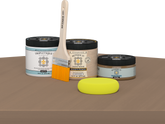 Retique It® Barn Wood Multipurpose Kit contents with Light Wood Liquid Wood primer, Barn Wood gel stain alternative, Tripletique matte interior top coat, paintbrush, and yellow sponge displayed on a wood surface.