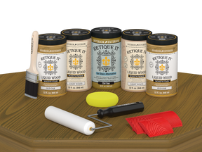 Retique It Old Oak Wood'n Kit featuring Old Oak Liquid Wood stain, Light Wood primer, Old Oak Gel Stain Alternative, paint brush, white roller, yellow sponge, and red graining tools displayed on a wood tabletop.