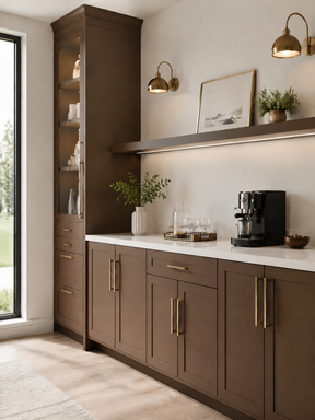 Modern kitchen and coffee bar with dark oak cabinetry, brass hardware and wall sconces, white countertop, black espresso machine, open shelving, and decorative greenery.